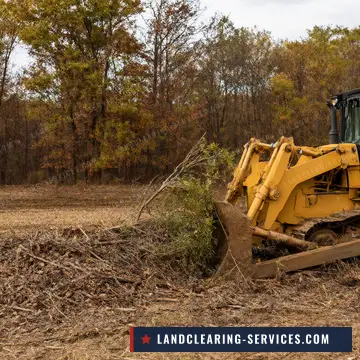 Crawler dozer pushing brush piles on a cleared field with fall hardwoods behind