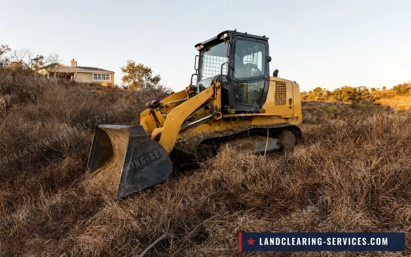 Track loader clearing dry grass and brush on a hillside below a house for defensible space