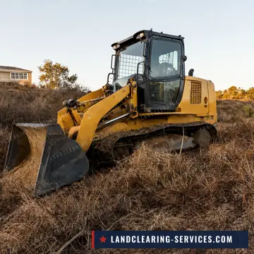 Track loader clearing dry grass and brush on a hillside below a house for defensible space